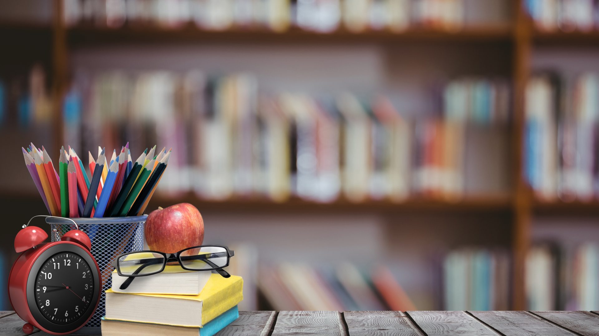 Primer plano de un lapicero y objetos de libreria con una biblioteca llena de libros de fondo.