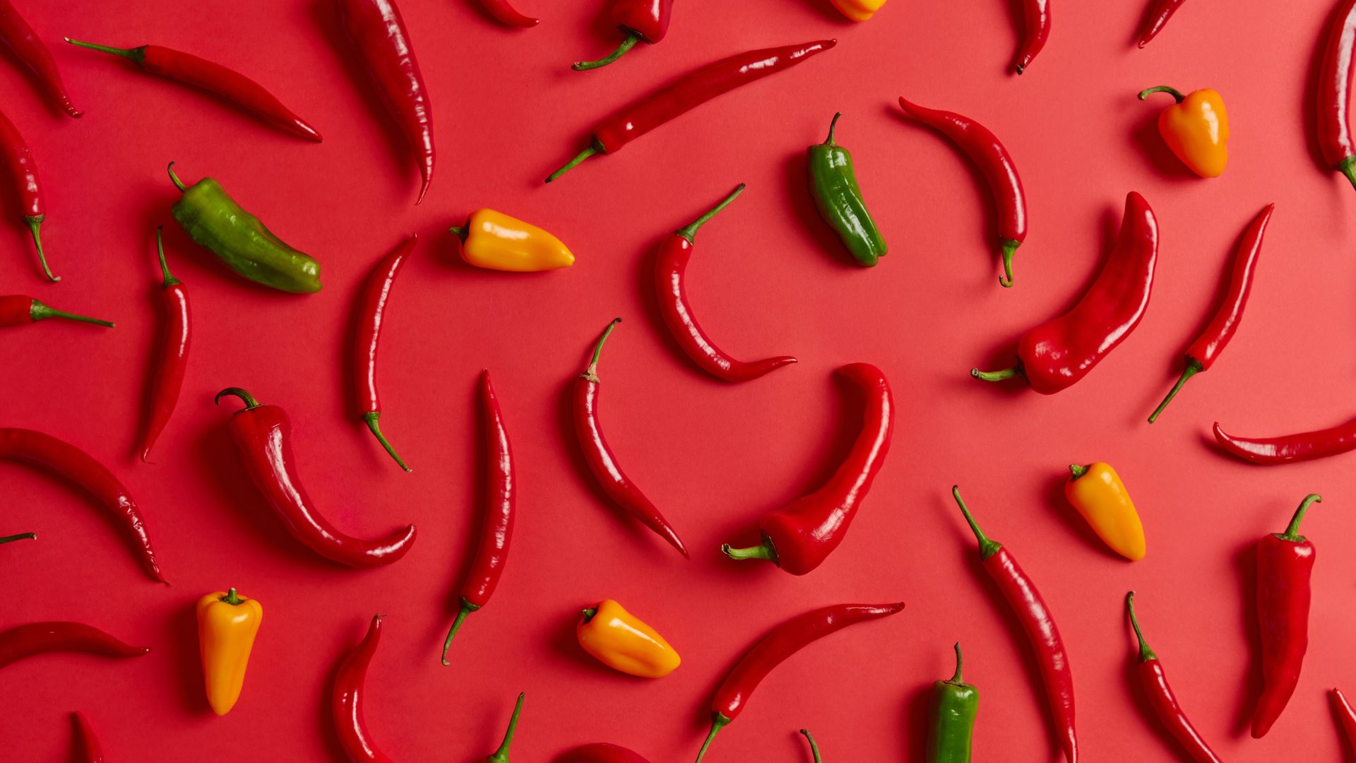 Chiles y jalapeños dispuestos en un fondo rojjo.