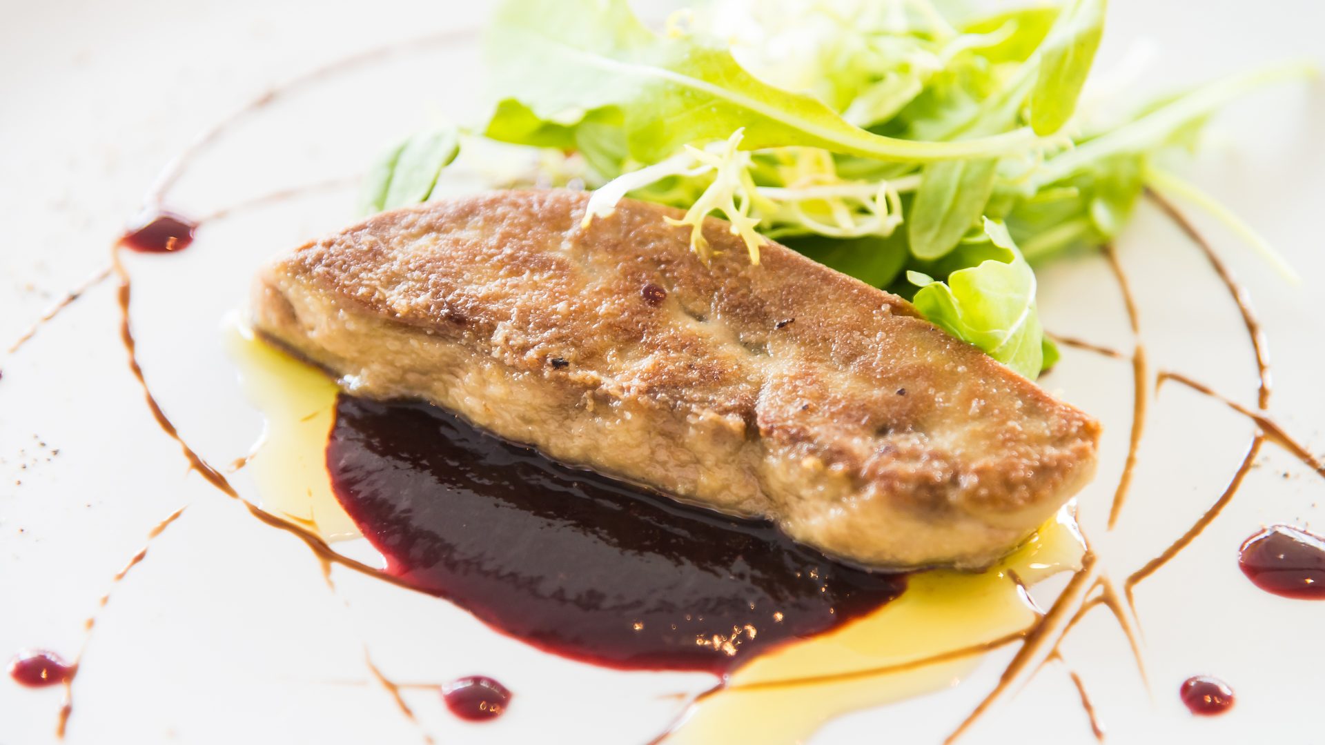 Foie gras a la parrilla emplatado con una salsa y verdes