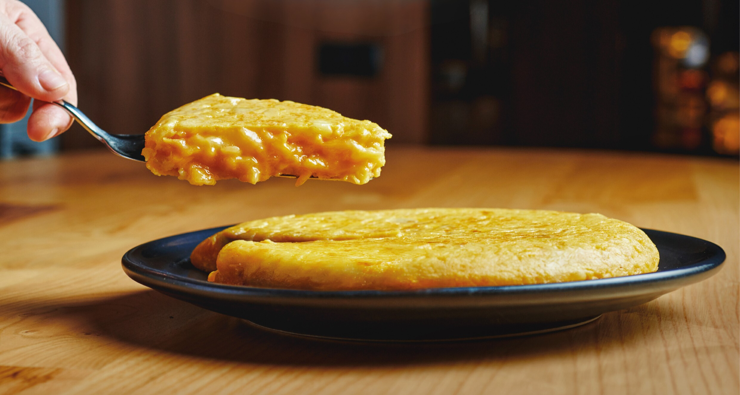 Tortilla de patatas en un plato y una persona cogiendo una proción